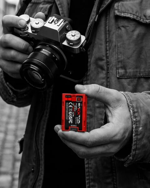 Fotograf in einer Altstadtgasse hält Kamera und einen roten Baxxtar NP-W235-Akku für Fujifilm