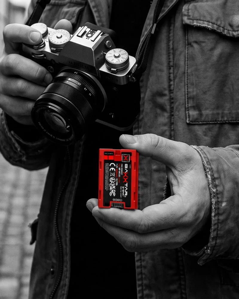 Fotograf in einer Altstadtgasse hält Kamera und einen roten Baxxtar NP-W235-Akku für Fujifilm
