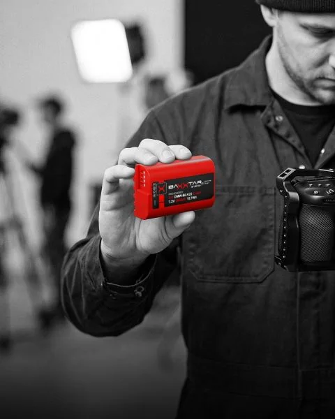 Videograf am Set hält Kamera mit Rig und einen roten Baxxtar DMW-BLK22-Akku für Panasonic